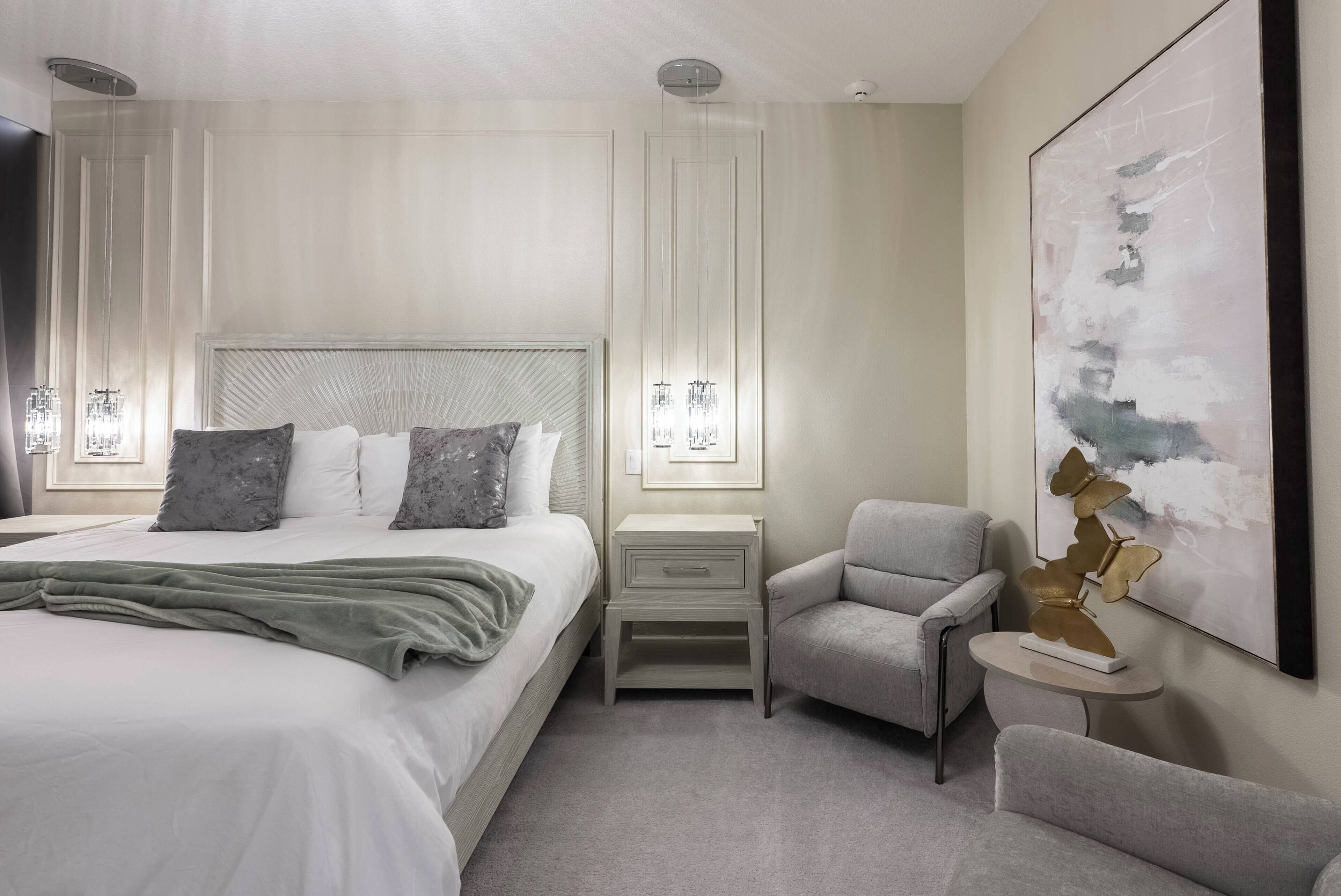 Un dormitorio moderno con una cama grande, mesitas de noche, una silla y una obra de arte colgada en la pared.