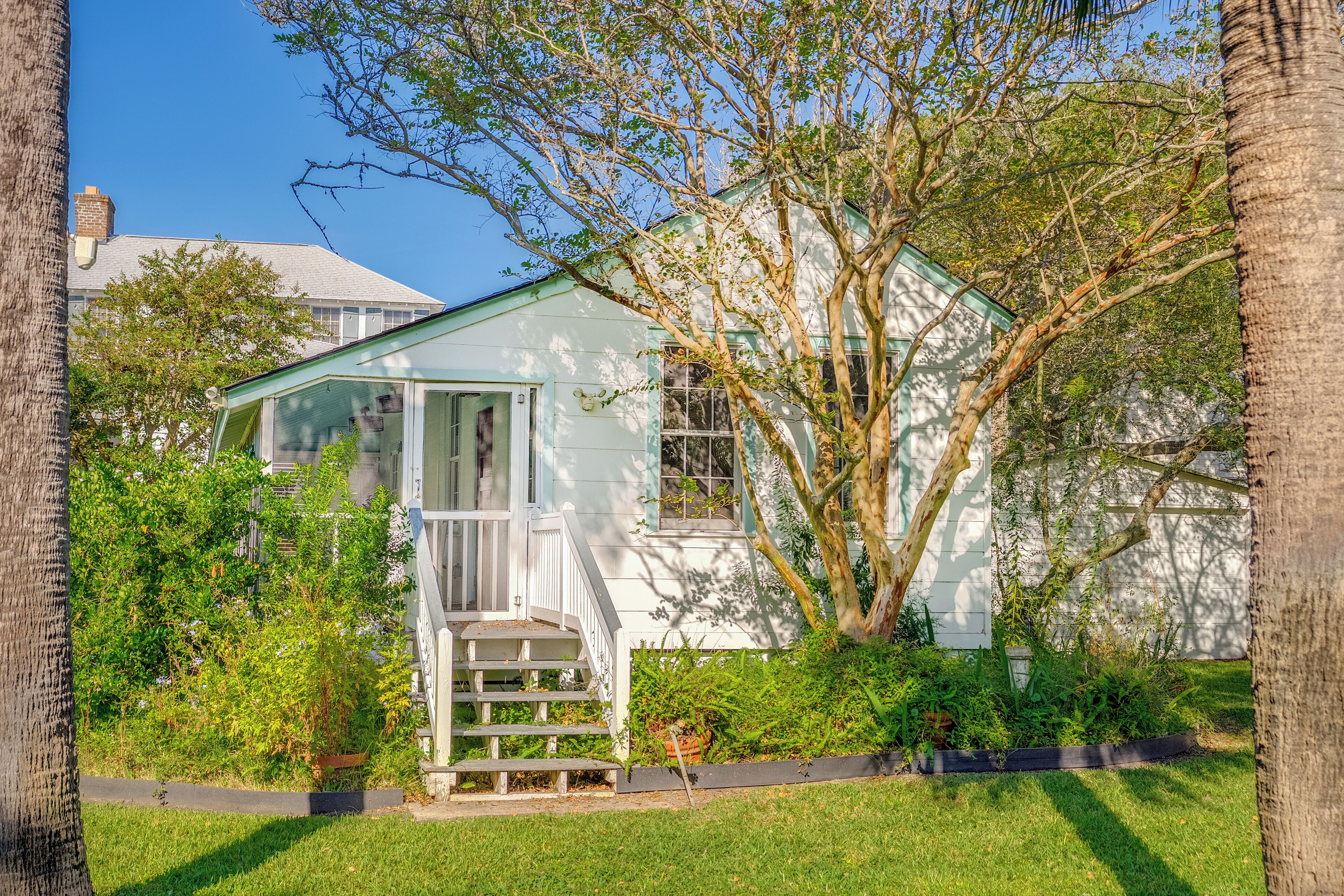A white house with a porch and steps, surrounded by greenery and trees.