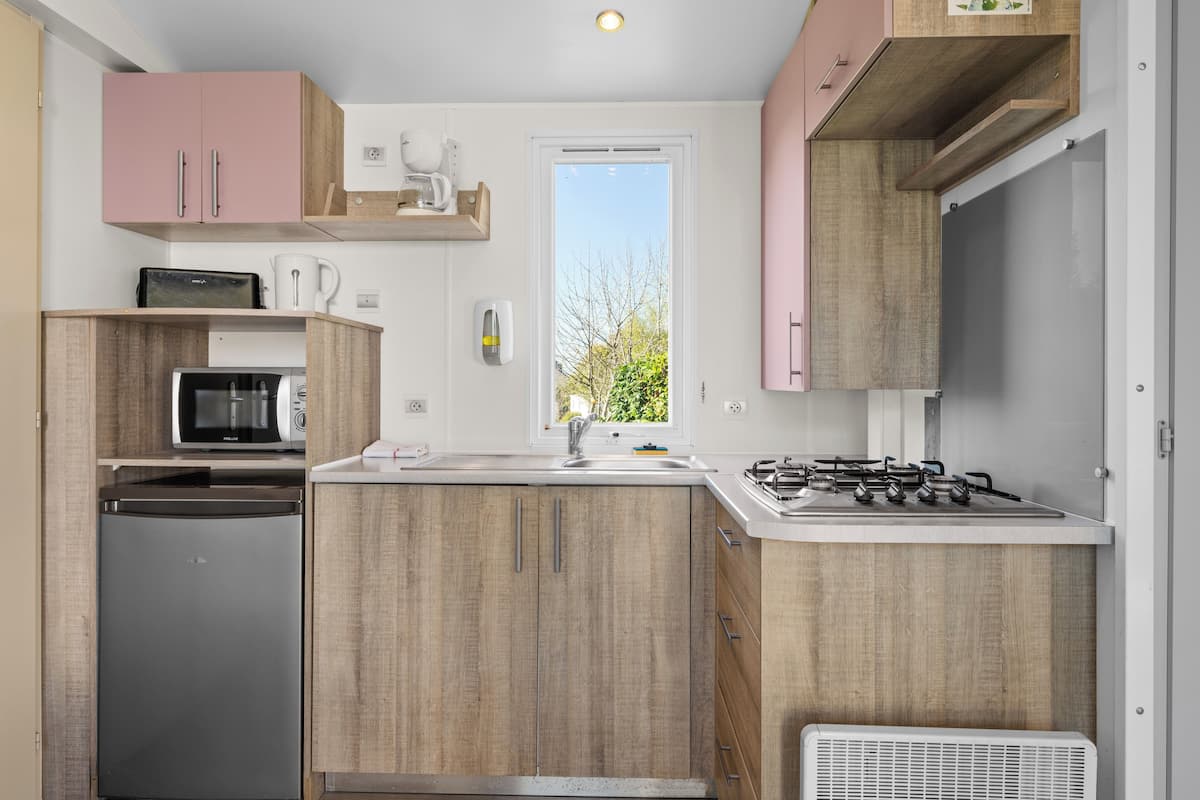 Een kleine keuken met een koelkast, magnetron, spoelbak en gasfornuis.