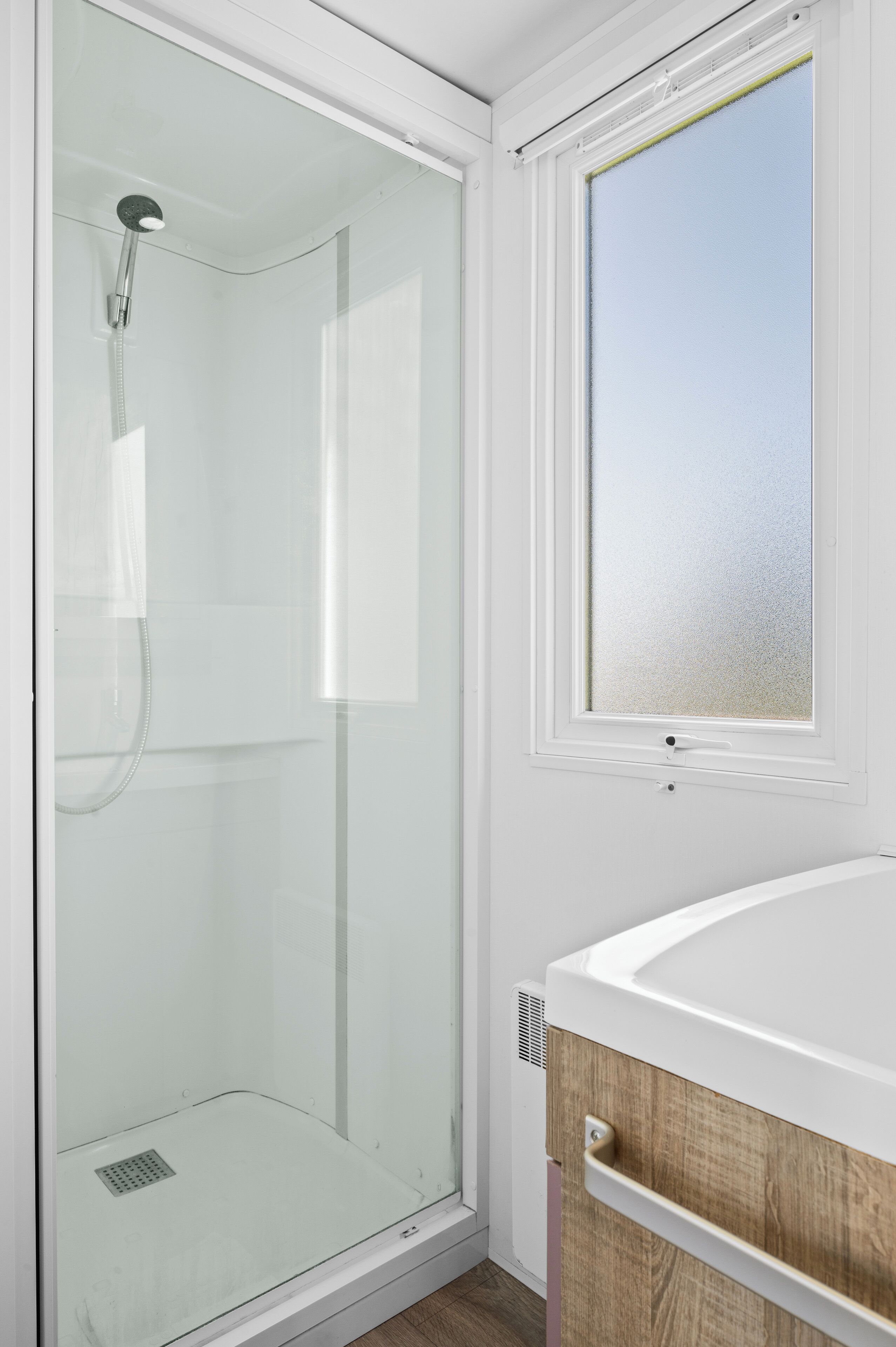 A modern bathroom with a glass-enclosed shower, a white sink, and a window with frosted glass.