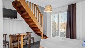 Een slaapkamer met een houten trap, een bed, een eettafel met stoelen, en een aan de muur bevestigde televisie.