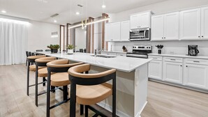 A modern kitchen with white cabinets, a central island with bar stools, and built-in appliances.