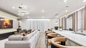A modern kitchen with a long island, bar stools, and a large window with sheer curtains.