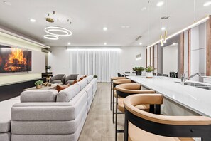 Una cocina moderna con una isla grande, taburetes de bar y un ventanal con cortinas traslúcidas.