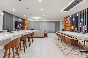Cozinha moderna com ilha central, banquetas de bar e área de jantar com mesa comprida e cadeiras.