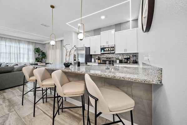A modern kitchen with a granite countertop, stainless steel appliances, and a bar area with bar stools. - 5BR house sleeps 16 with spa in kissimmee (Kissimmee)