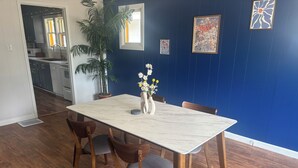 Un comedor con una mesa de mármol, sillas de madera, un florero con flores y una pared azul decorada con cuadros.