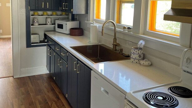 Una cocina con armarios azul oscuro, encimera blanca, pileta de acero inoxidable y estufa integrada.
