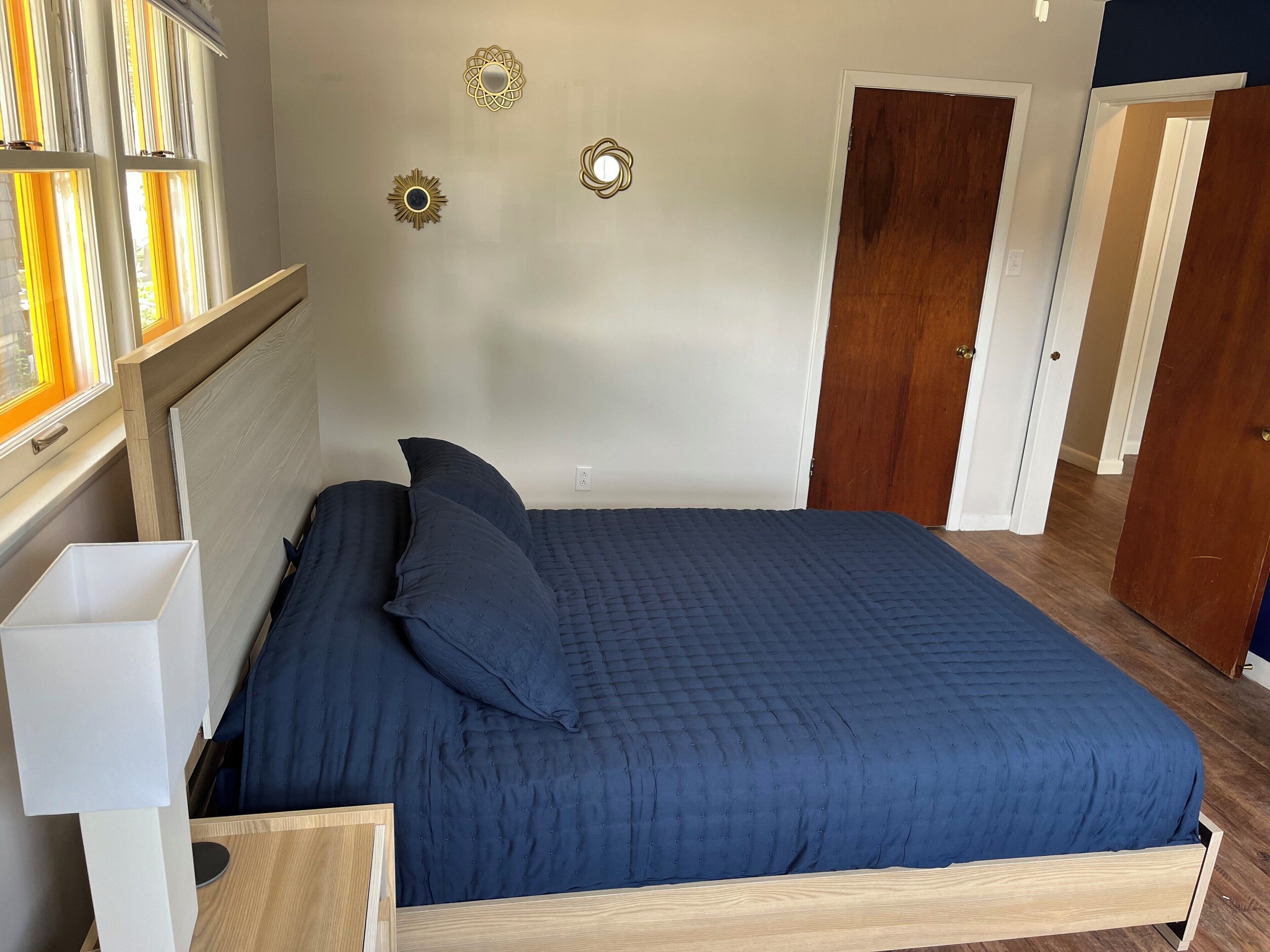 Ein Schlafzimmer mit einem Bett, einem Nachttisch, einer Lampe und einem Fenster mit Vorhängen.