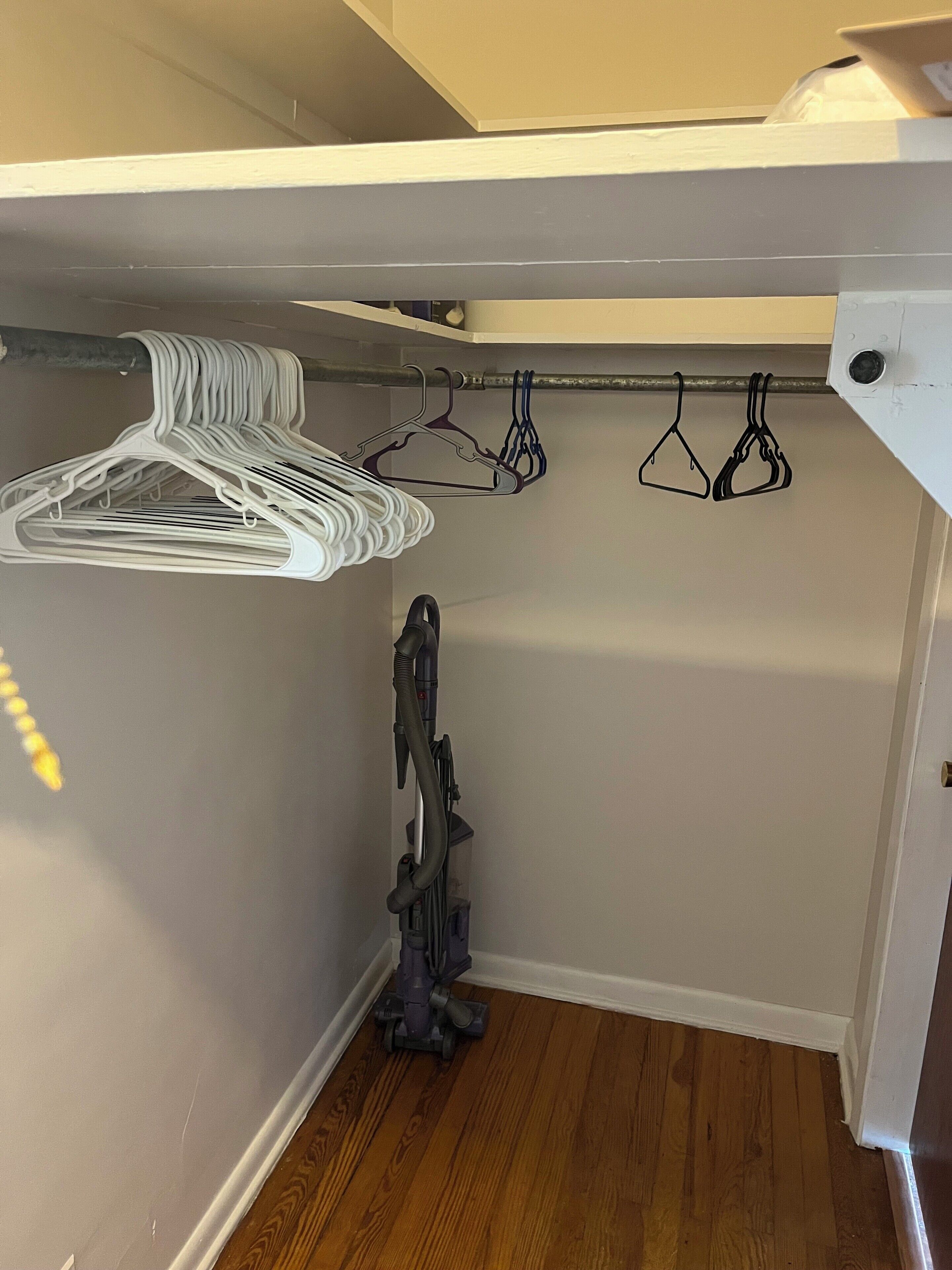 Un placard avec des cintres blancs et un aspirateur.