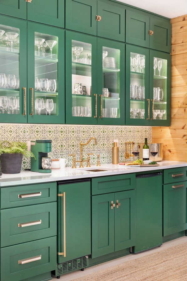 A kitchen with green cabinets, glass-fronted shelves holding wine glasses, a coffee maker, and a sink with gold fixtures. - Luxury Cabin Getaway in the Blue Ridge Mountains (Fort Valley)