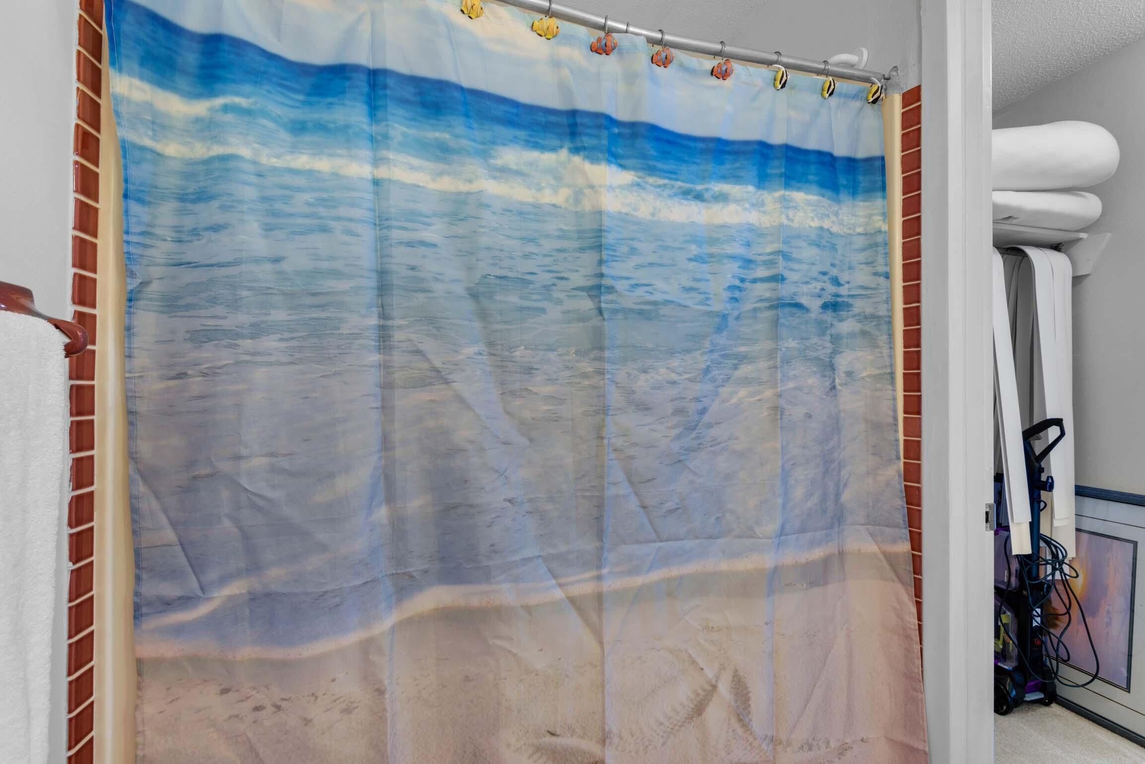 A bathroom with a beach-themed shower curtain, a white towel rack, and a visible power outlet.