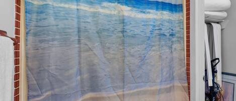 A bathroom with a beach-themed shower curtain, a white towel rack, and a visible power outlet.