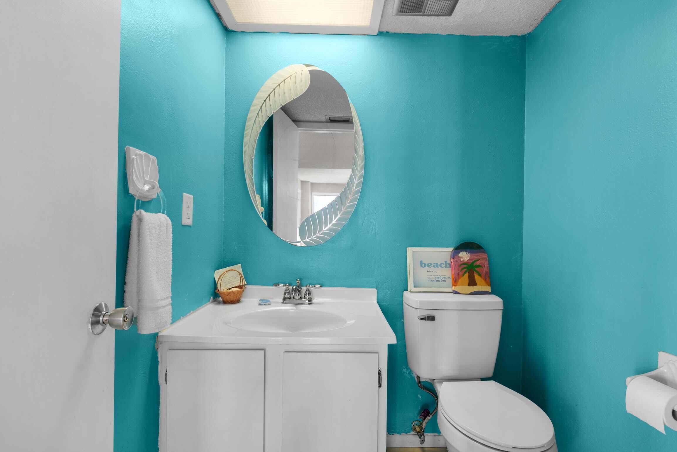 Een badkamer met een witte wastafel, toilet en een spiegel met bladmotief.