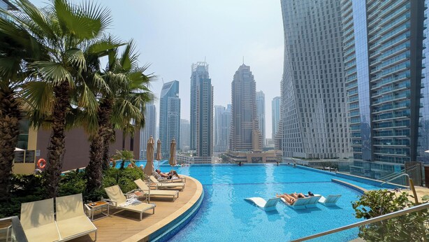 A swimming pool with lounge chairs and palm trees, surrounded by tall buildings.