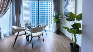 A modern dining area with a glass table, white chairs, and a view of tall buildings through large windows.