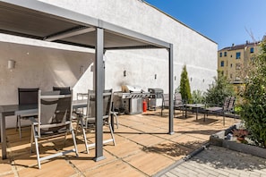 Un patio exterior con una parrilla, asientos y una estructura de pérgola.