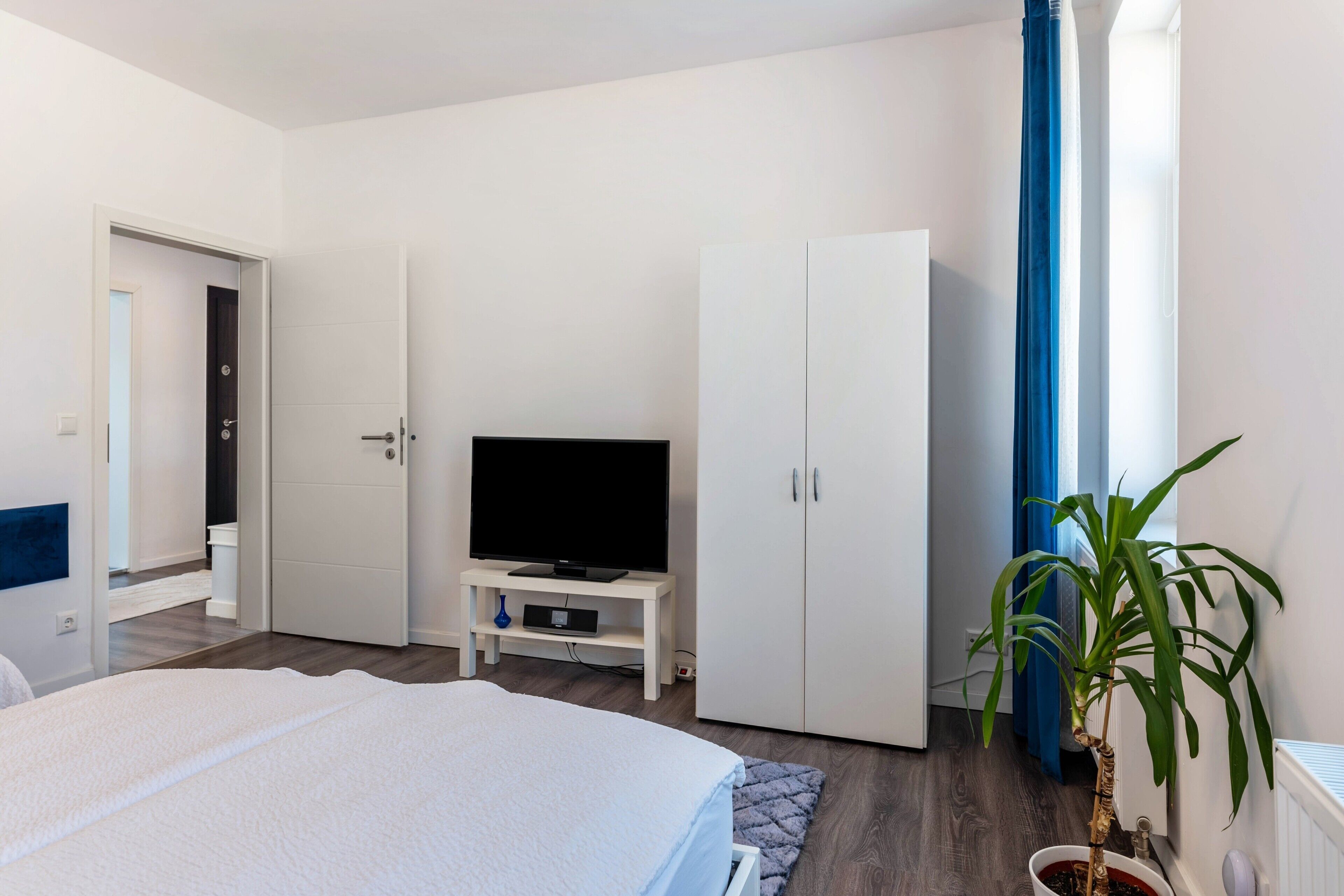 A bedroom with a bed, a television on a stand, a wardrobe, and a potted plant.