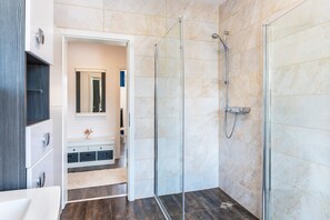 A modern bathroom with a glass-enclosed shower, a vanity with a mirror, and a small decorative vase.
