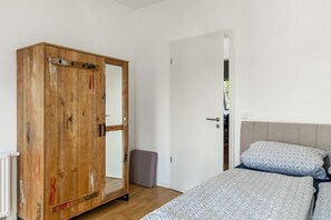 Un dormitorio con un armario de madera, una cama con ropa de cama estampada y vistas a través de una puerta abierta.