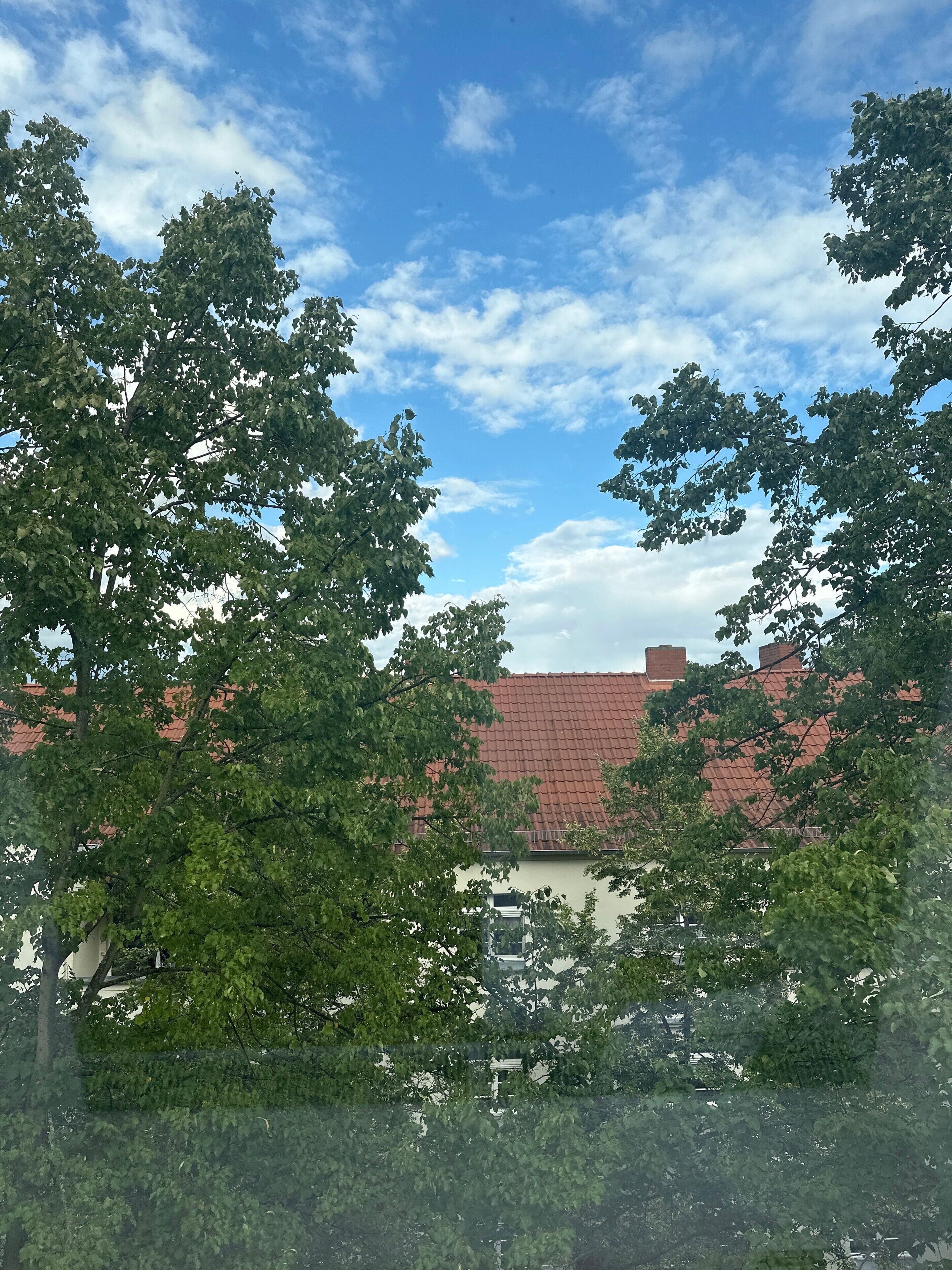 Ein Gebäude mit rotem Ziegeldach, teilweise von Bäumen verdeckt.