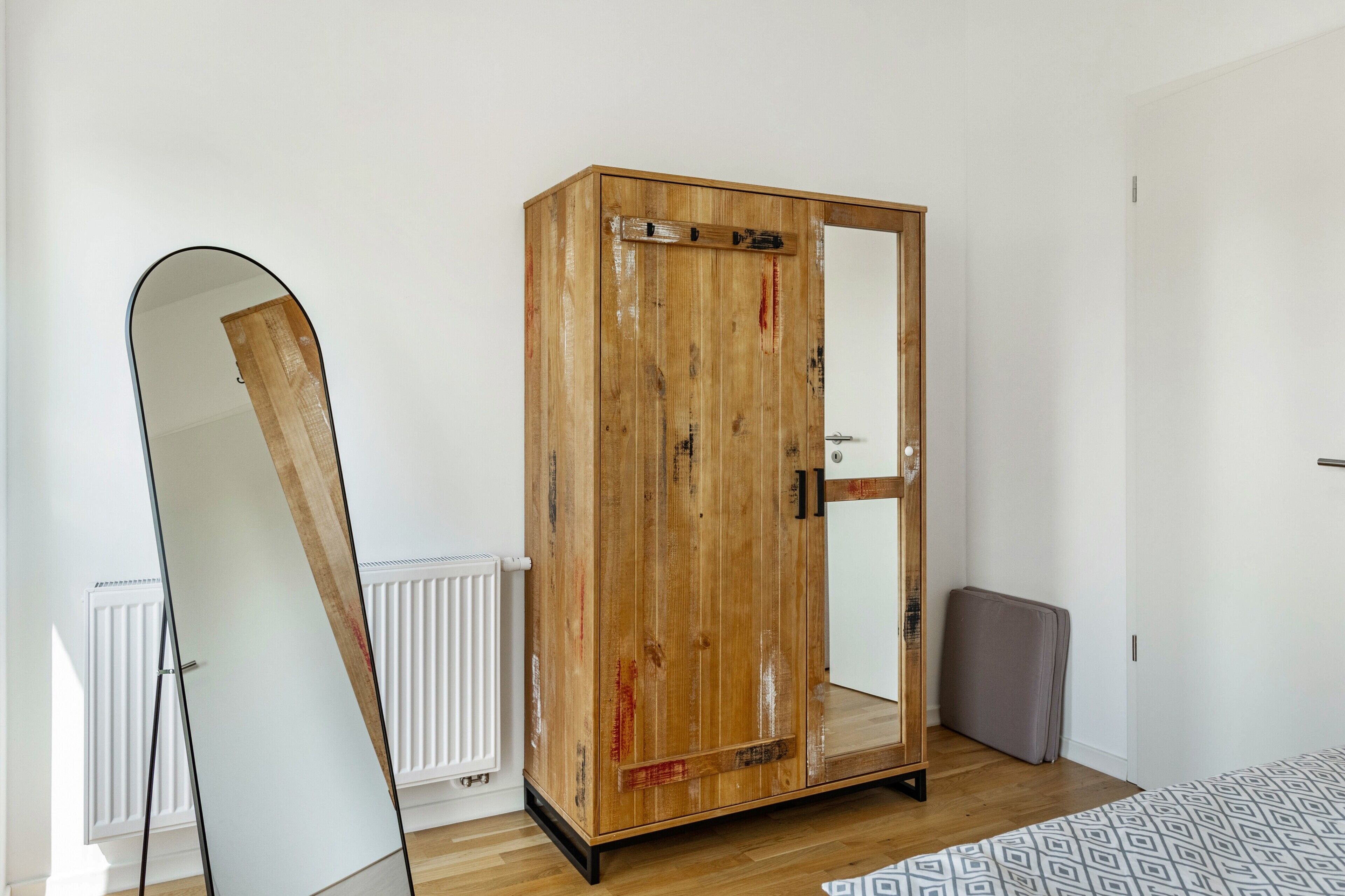 A room with a wooden wardrobe, a mirror, a radiator, and a patterned rug.