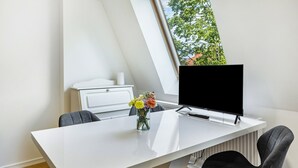Een moderne kantoorruimte met een wit bureau, twee grijze stoelen, een computerscherm en een vaas met bloemen.