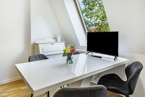 Et moderne kontor med et hvidt skrivebord, to grå stole, en computerskærm og en vase med blomster.