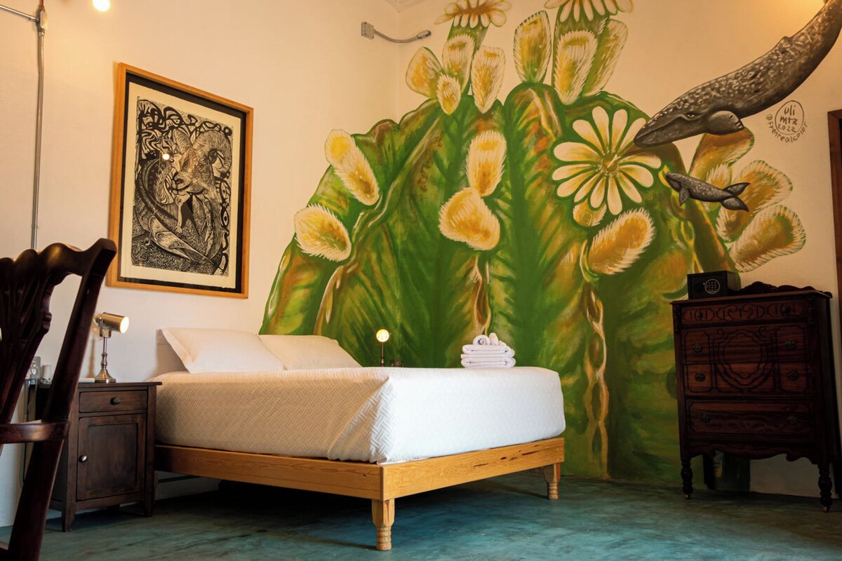 A bedroom with a bed, a nightstand, a dresser, a framed artwork, and a mural.