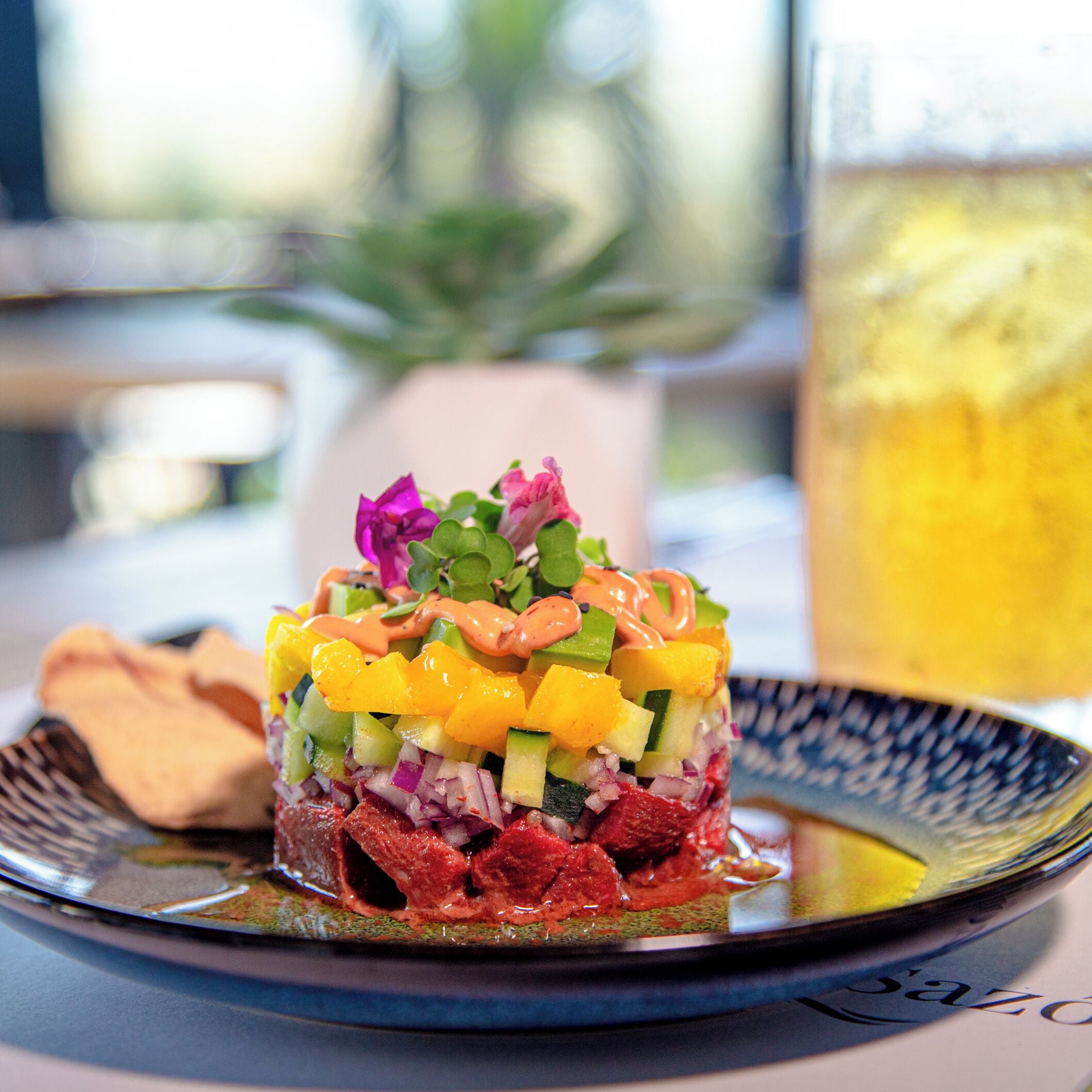 Ensalada colorida en capas sobre un plato, con una bebida al fondo.