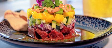 Ensalada colorida en capas sobre un plato, con una bebida al fondo.