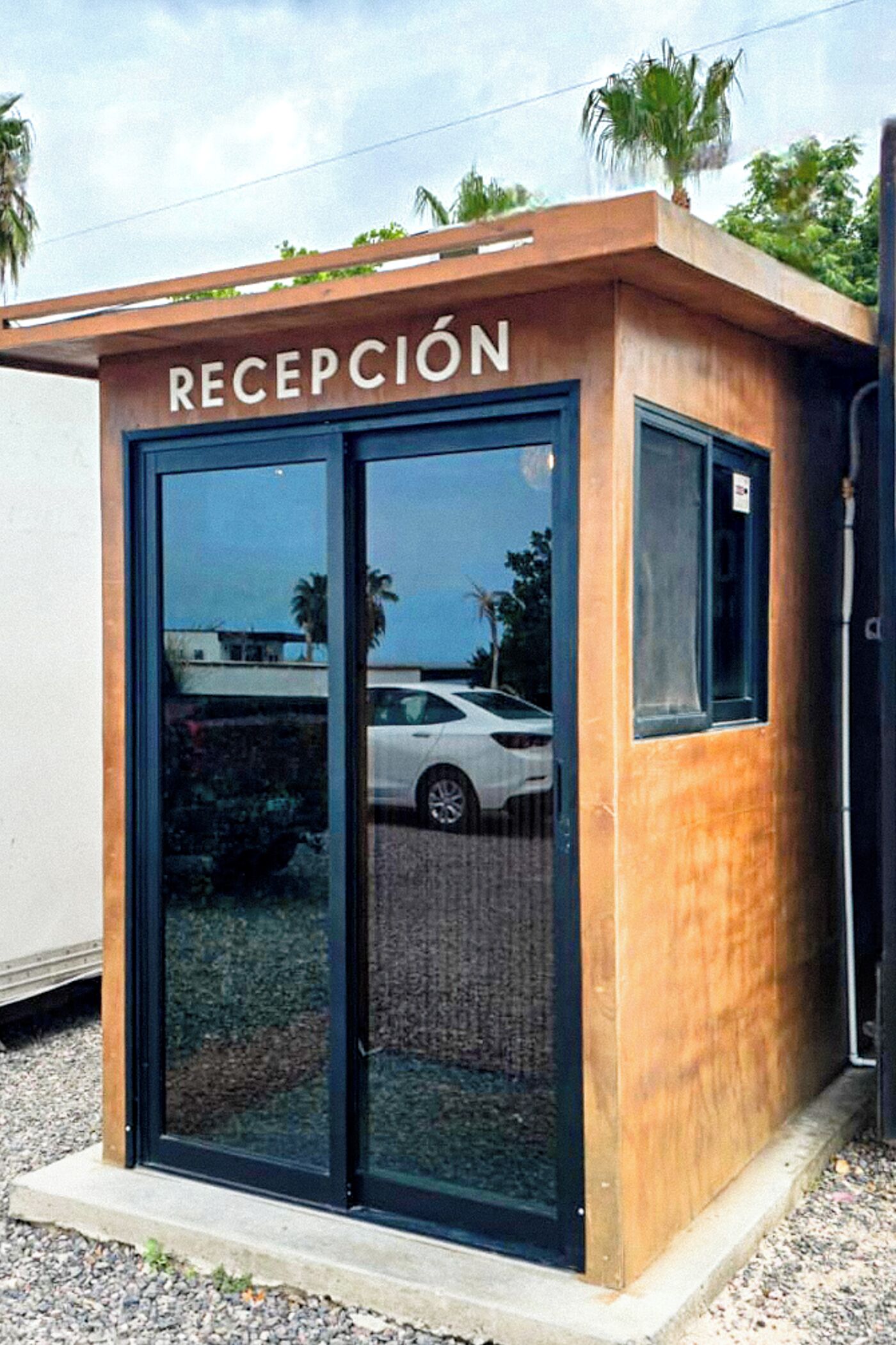 A reception area with a wooden exterior and glass doors, featuring a sign that reads "RECEPCIÓN".