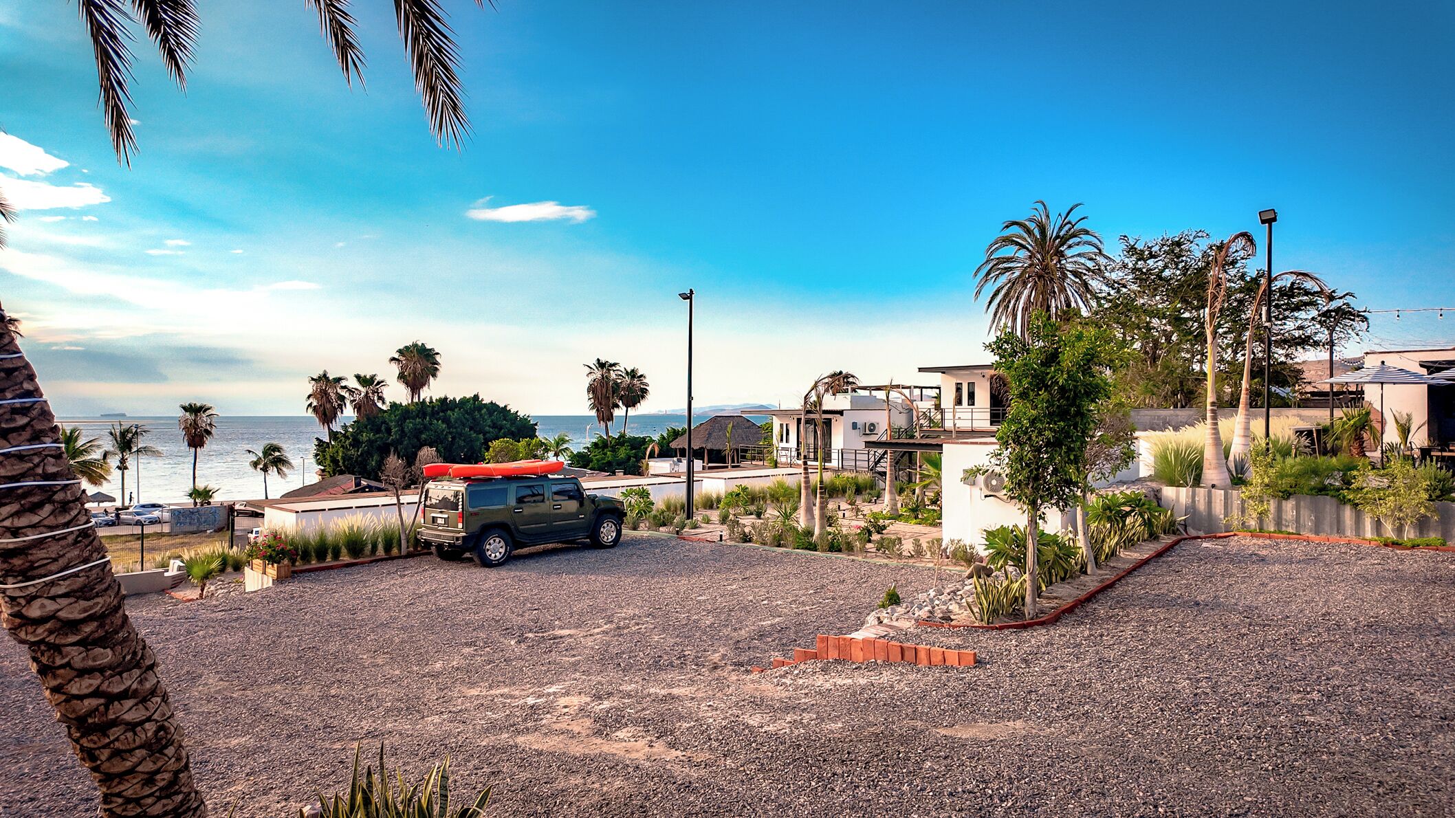 A residential area with a parked SUV, palm trees, and a view of the ocean.