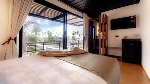 Een slaapkamer met een groot bed, een aan de muur bevestigde televisie en een balkon met uitzicht op palmbomen.
