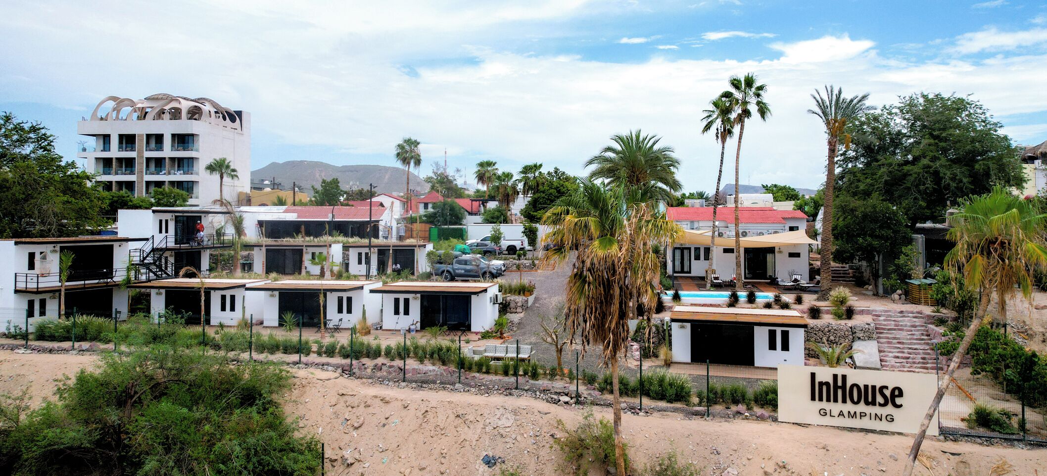 Zona residencial con varias casas blancas, una piscina y un letrero que dice 'InHouse GLAMPING'.