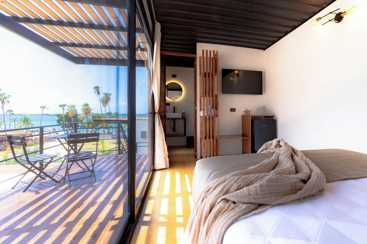 A modern hotel room with a balcony, a bed, a TV, and a minibar.