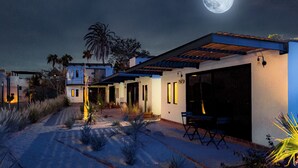 Een modern huis met een terras, grote ramen en een maan aan de hemel.