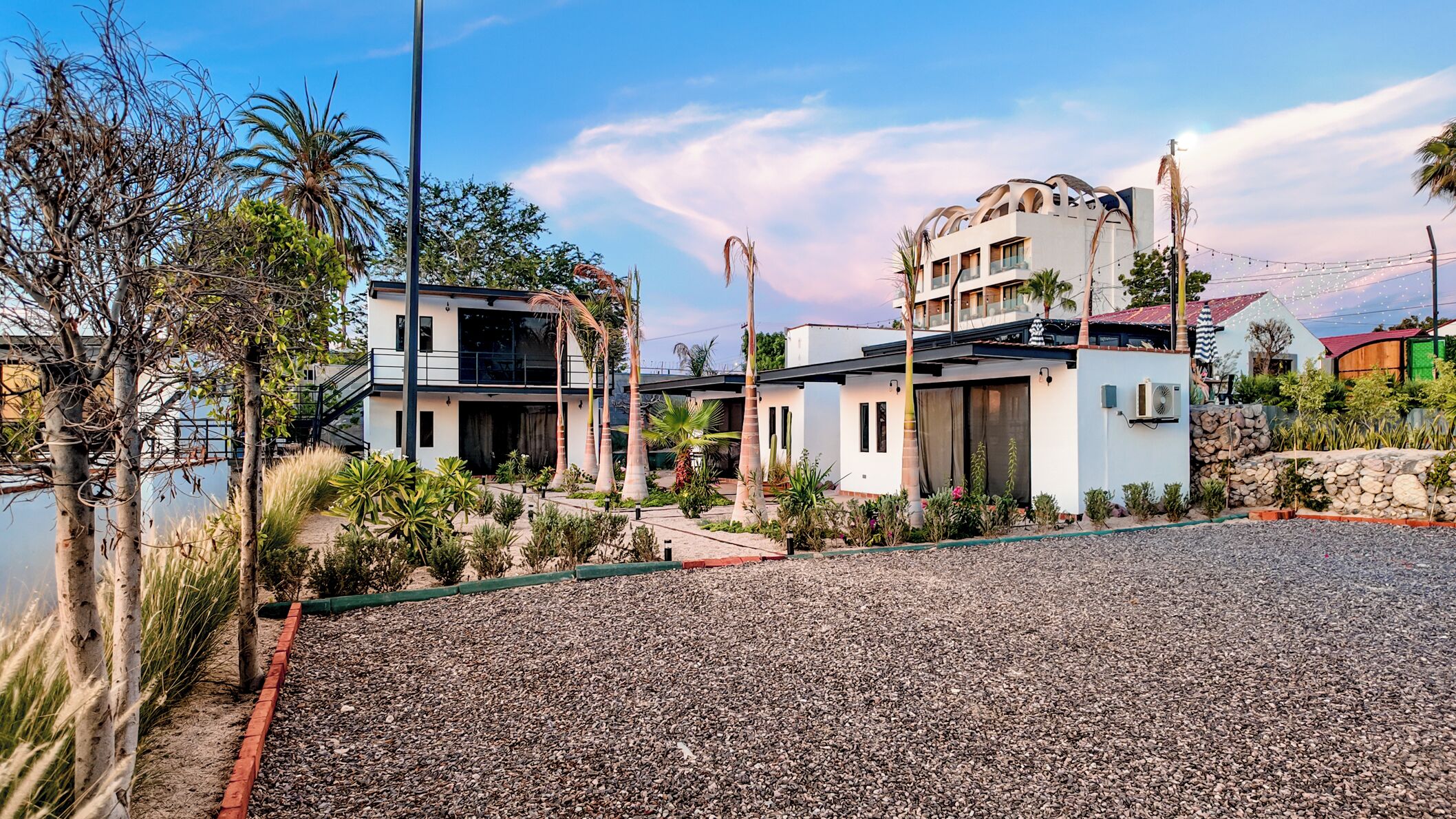 A modern two-story building with a balcony, a covered patio, and a gravel driveway.