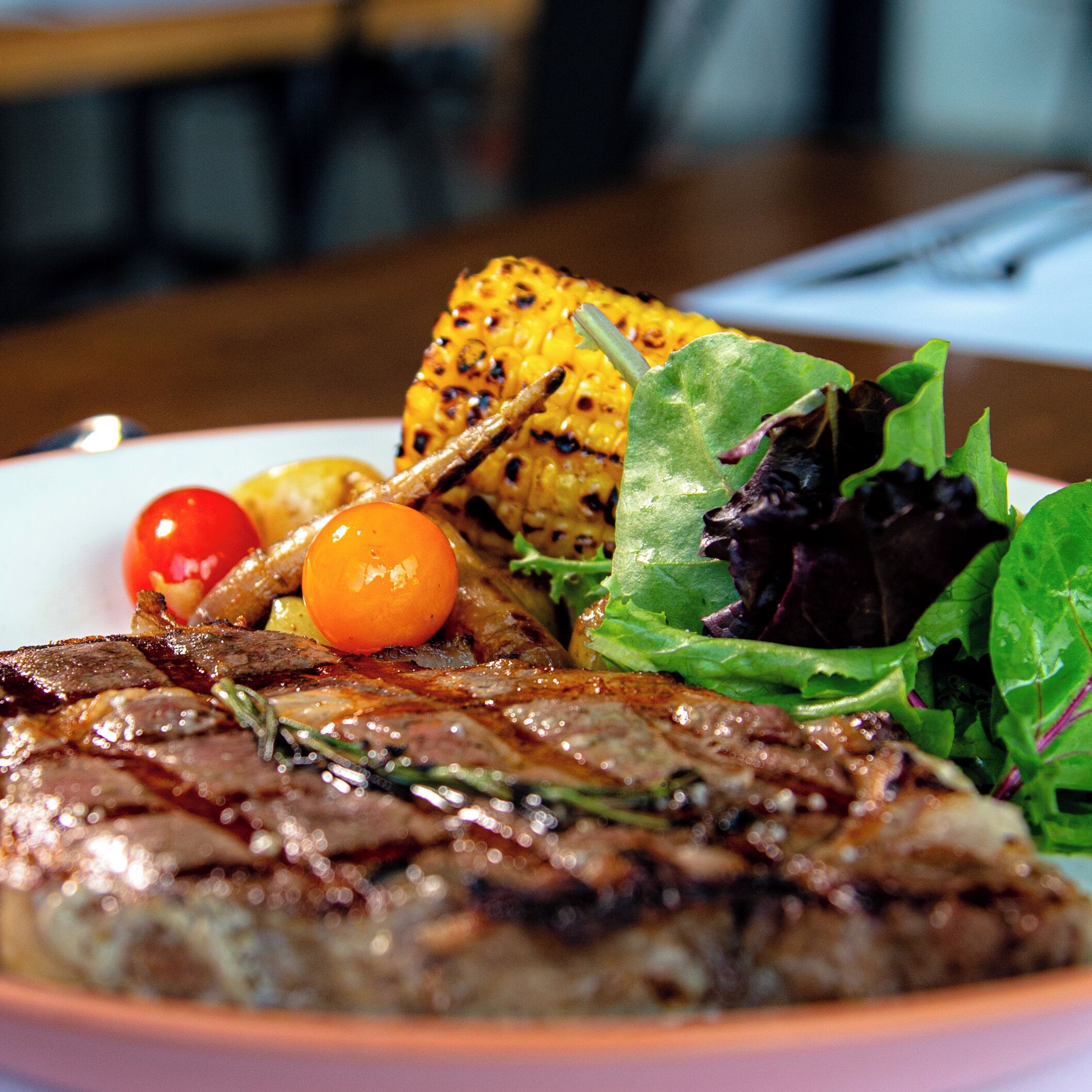 A plate with grilled meat, grilled corn, cherry tomatoes, and a salad.