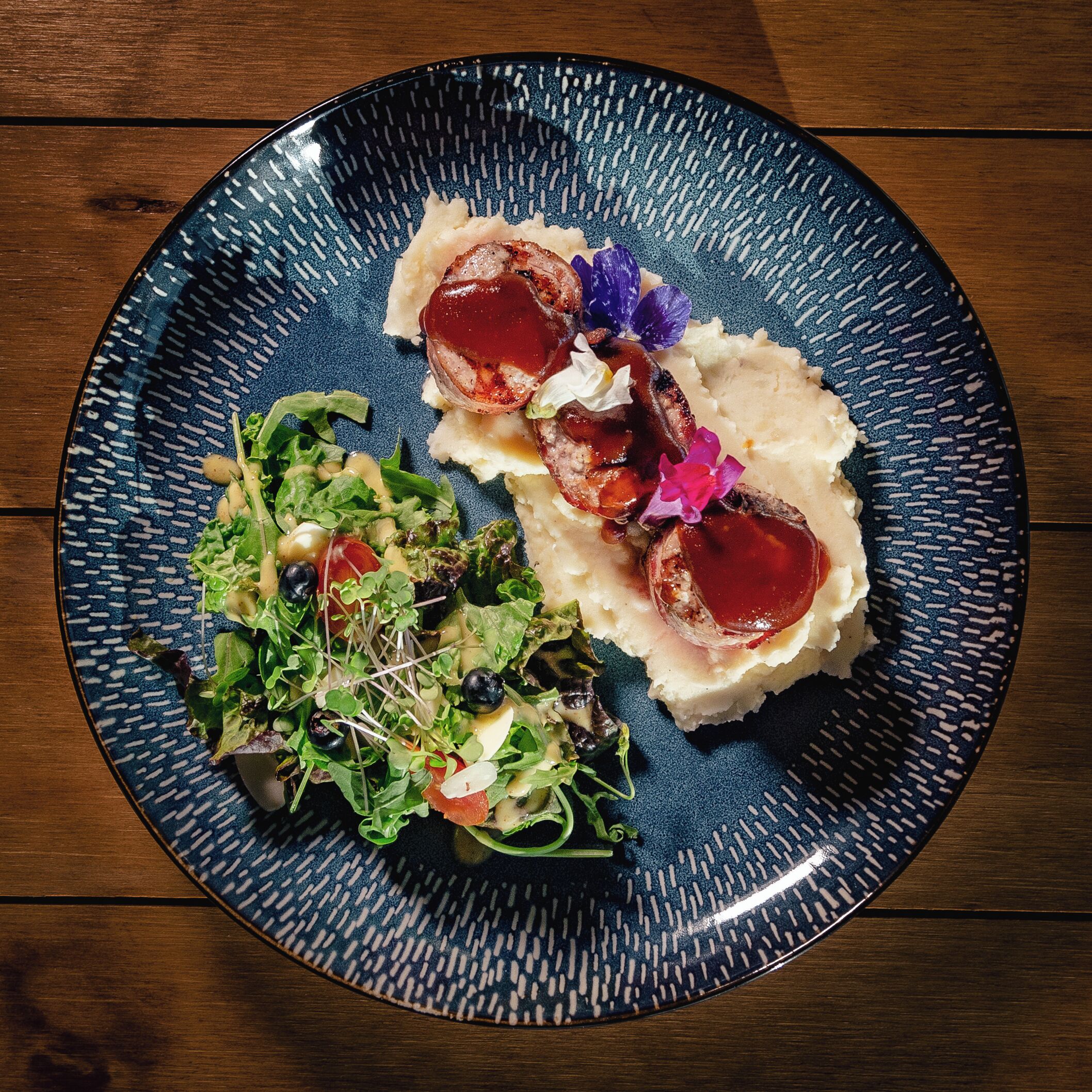 A plate with a meat dish, mashed potatoes, and a mixed greens salad.