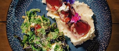 A plate with a meat dish, mashed potatoes, and a mixed greens salad.