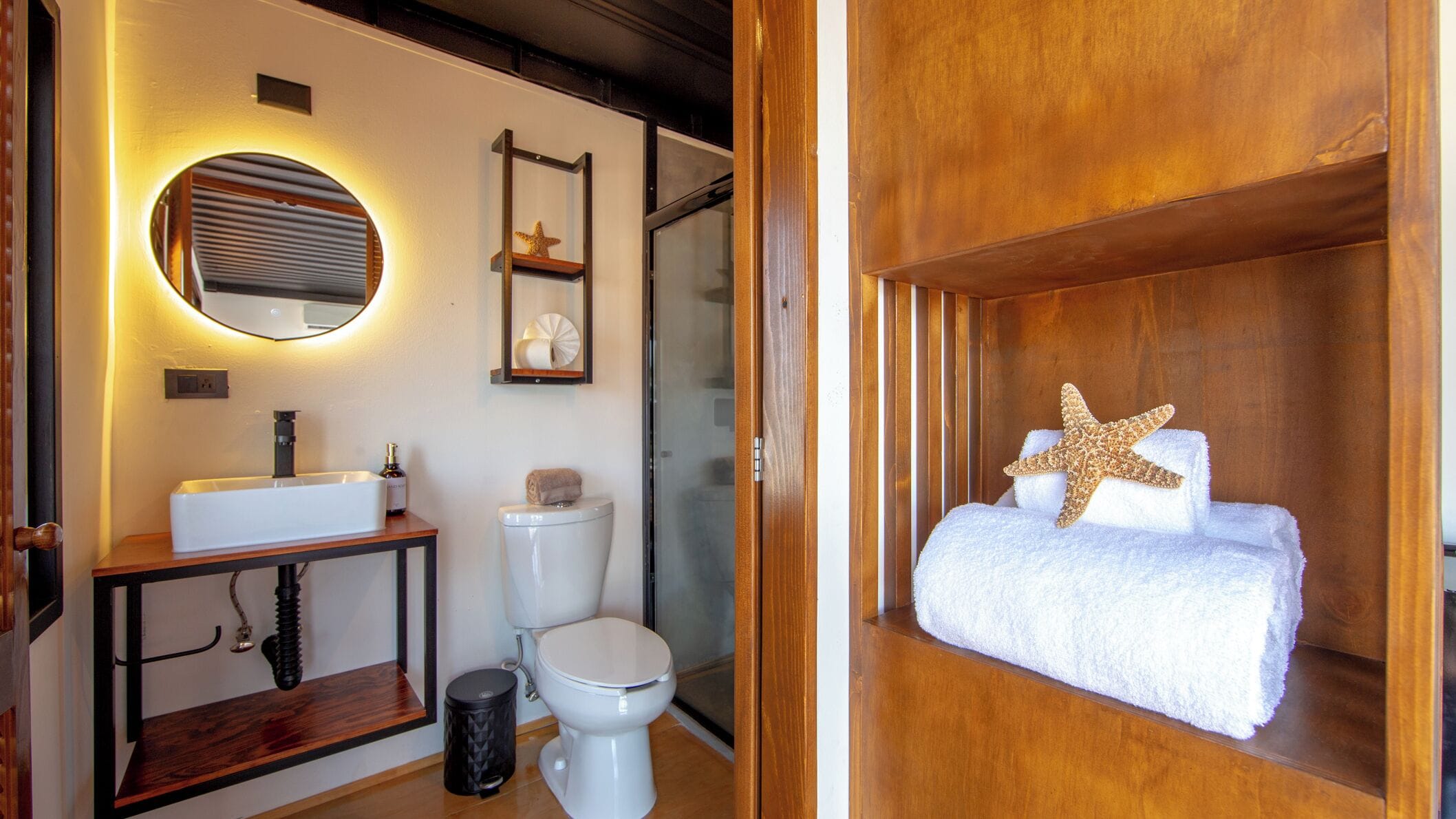 Ein modernes Badezimmer mit Waschtisch aus Holz, einem runden Spiegel, einer Toilette und einer Duschkabine.