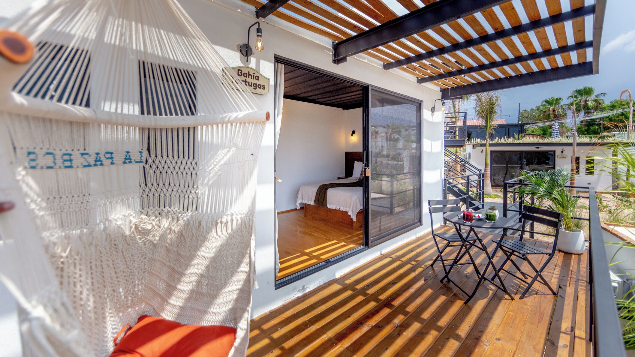 Una habitación moderna con cama, una hamaca y balcón con mesa y sillas.