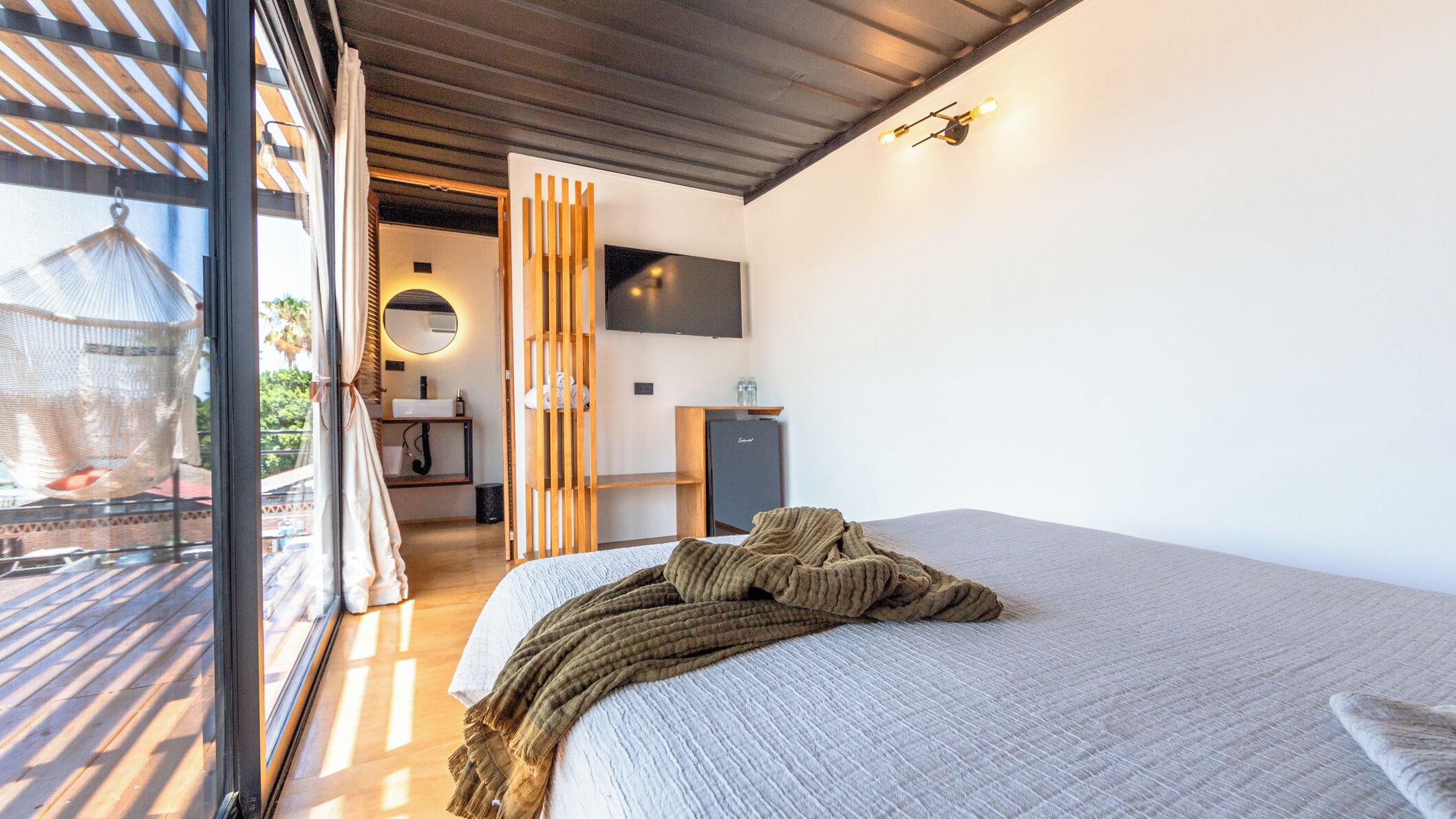 Un dormitorio moderno con una cama grande, un televisor en la pared y un balcón con una silla colgante.