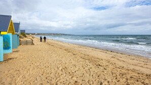 Una playa arenosa con algunas personas caminando, una cerca de madera y un edificio de fachada azul y amarilla.