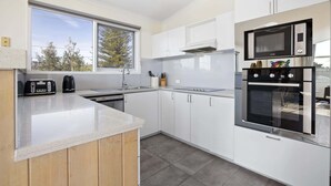 Una cocina moderna con armarios blancos, horno empotrado, microondas y lavavajillas.