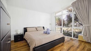 Un dormitorio con una cama, una mesita de noche, una lámpara y un ventanal con cortinas.