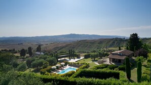 A villa with a swimming pool, surrounded by lush gardens and a scenic hillside view.