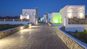 Un chemin menant à un bâtiment moderne aux murs en pierre et aux lumières vertes illuminées.