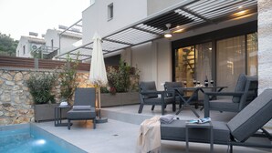 Un patio moderno al aire libre con piscina, sillas de descanso y una zona de comedor con mesa y sillas.